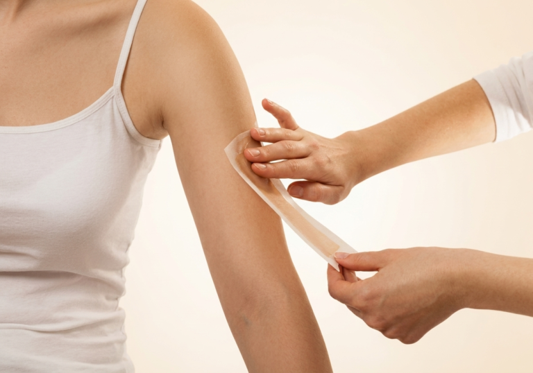A beauty therapist applying a professional arm wax strip for smooth skin during a body hair removal offer at Margarita Salon in Sharjah.
